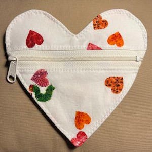 May include: White heart-shaped zippered pouch with a colorful caterpillar and red, orange, and brown hearts printed on it.