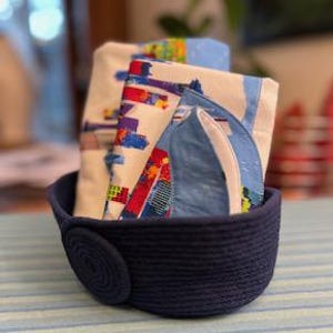 May include: A set of three blue and white patterned baby washcloths in a navy blue rope basket with a large button.