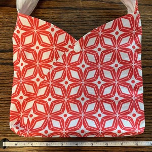 May include: A red and white fabric tote bag with a geometric pattern of stars. The bag has a white button closure and is approximately 9 inches wide.