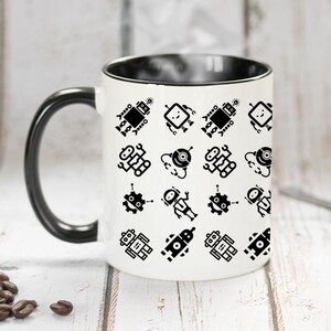 May include: A white ceramic mug with a black rim and handle. The mug features a repeating pattern of black robot illustrations.