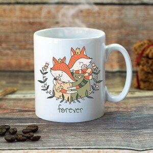 Puede incluir: Taza de cer&aacute;mica blanca con un dise&ntilde;o de dos zorros abraz&aacute;ndose, uno con una corona y el otro con una bufanda. Los zorros est&aacute;n rodeados de hojas verdes y flores. La taza tiene la palabra "forever" impresa en la parte inferior.