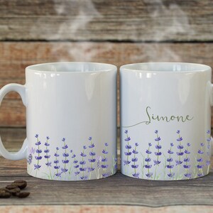 May include: Two white ceramic mugs with lavender floral designs. One mug has the name "Simone" written on it.