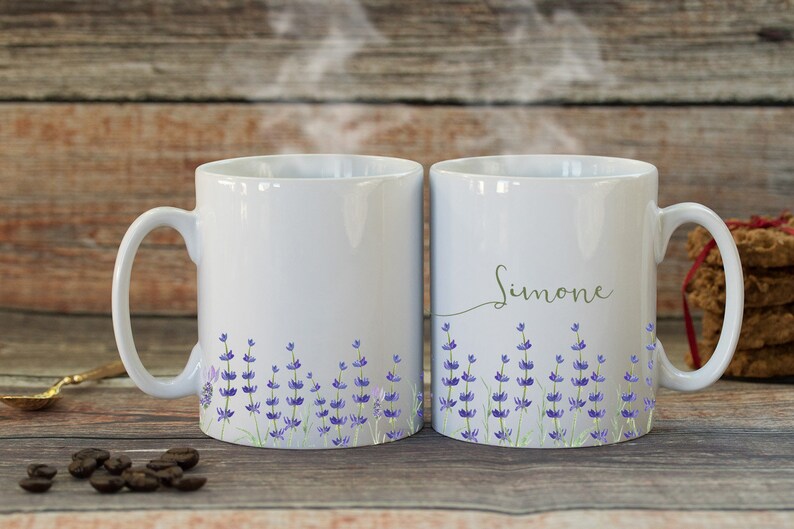 May include: Two white ceramic mugs with lavender floral designs. One mug has the name "Simone" written on it.
