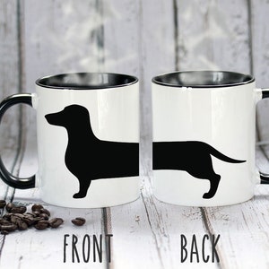 May include: White ceramic mug with a black interior and handle. The mug features a black silhouette of a dachshund dog. The word "FRONT" is printed below the front view of the dog, and "BACK" is printed below the back view.