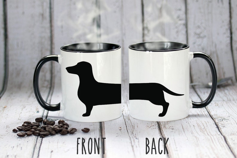 May include: White ceramic mug with a black interior and handle. The mug features a black silhouette of a dachshund dog. The word "FRONT" is printed below the front view of the dog, and "BACK" is printed below the back view.