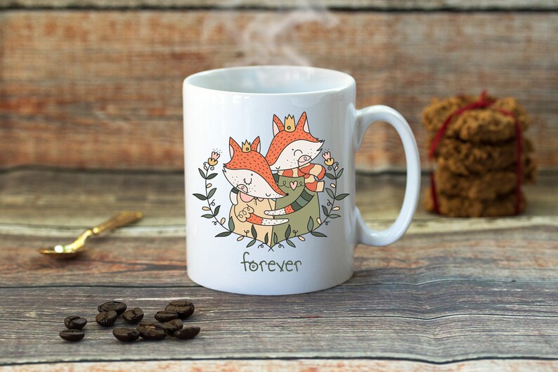 Puede incluir: Taza de cer&aacute;mica blanca con un dise&ntilde;o de dos zorros abraz&aacute;ndose, uno con una corona y el otro con una bufanda. Los zorros est&aacute;n rodeados de hojas verdes y flores. La taza tiene la palabra "forever" impresa en la parte inferior.