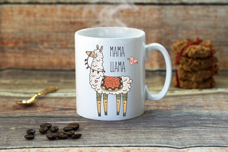Puede incluir: Taza de cer&aacute;mica blanca con una ilustraci&oacute;n de llama de dibujos animados y el texto "Mama Llama". La llama lleva una manta de patrones coloridos y tiene un coraz&oacute;n rosa sobre su cabeza.