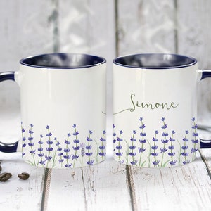 May include: Two white ceramic mugs with blue rims and handles. One mug has the name "Simone" written in cursive on the front. Both mugs feature a lavender floral design.