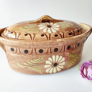 May include: A brown ceramic oval baking dish with a lid. The dish is decorated with a floral pattern in shades of brown, green, and white.