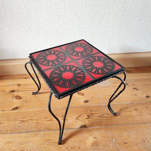 May include: A small square side table with a black metal frame and a red and black tiled top. The tiles have a geometric pattern.