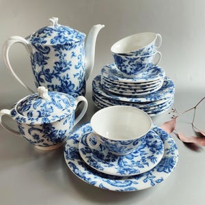 Puede incluir: Juego de té de porcelana con un estampado floral azul. El juego incluye una tetera, azucarero, tazas y platillos. El juego de té es blanco con un diseño floral azul.