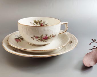 May include: A white teacup and saucer set with a floral pattern. The cup has a gold rim and the saucer has a gold trim. The set is made of porcelain.