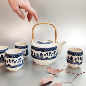 May include: A blue and white tea set with a teapot and four cups. The teapot has a bamboo handle and the cups have a blue and white floral pattern.