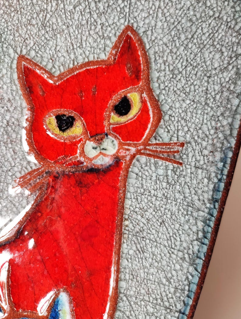 May include: A red cat illustration with yellow eyes and white whiskers. The cat is set against a textured, light gray background with a cracked pattern. The artwork has a handmade, folk art style.