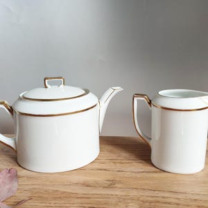 May include: A white teapot and creamer set with gold trim. The teapot has a lid and a spout. The creamer has a handle and a spout.