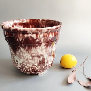 May include: A ceramic planter featuring a glossy, marbled glaze in deep chocolate brown and creamy white. The vessel has a wide, flared rim and horizontal ridges along its body, creating a textured appearance with a distinct drip pattern.