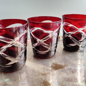 Peut inclure: Trois verres à boire en verre rouge avec un motif clair en forme de croix. Les verres sont posés sur un plateau argenté.