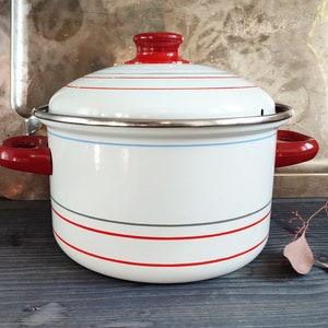 Peut inclure: Une casserole en émail blanc avec des rayures rouges et bleues et un couvercle rouge. La casserole a deux poignées rouges.