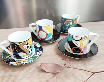 May include: Set of four colourful espresso cups and saucers with geometric and clock designs. The cups and saucers are white with black, yellow, blue, green, and red accents.