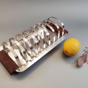 Könnte beinhalten: Ein silberfarbener Toaster mit dunklem Holzsockel. Der Ständer hat gewölbte Trennwände und eine rechteckige Form. Eine gelbe Zitrone liegt daneben. Dies ist ein Küchenartikel.