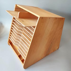 Könnte beinhalten: Ein hellfarbiger Schreibtisch-Organizer aus Holz mit mehreren abgewinkelten Schlitzen für Papiere und Dokumente. Der Organizer hat eine schräge Oberseite mit einem kleinen Regal und einem unteren Fach. Die Holzmaserung ist sichtbar, und das Design ist minimalistisch.