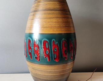 Puede incluir: Un jarrón de cerámica ovalado y alto, con un patrón de rayas horizontales texturizadas en tonos marrones y beige. Una banda turquesa con formas rojas abstractas rodea el jarrón. Acabado brillante.