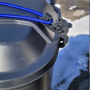 Puede incluir: Un cubo de basura de pl&aacute;stico negro con una cuerda azul atada alrededor de la tapa. La tapa tiene un cierre de pl&aacute;stico negro.