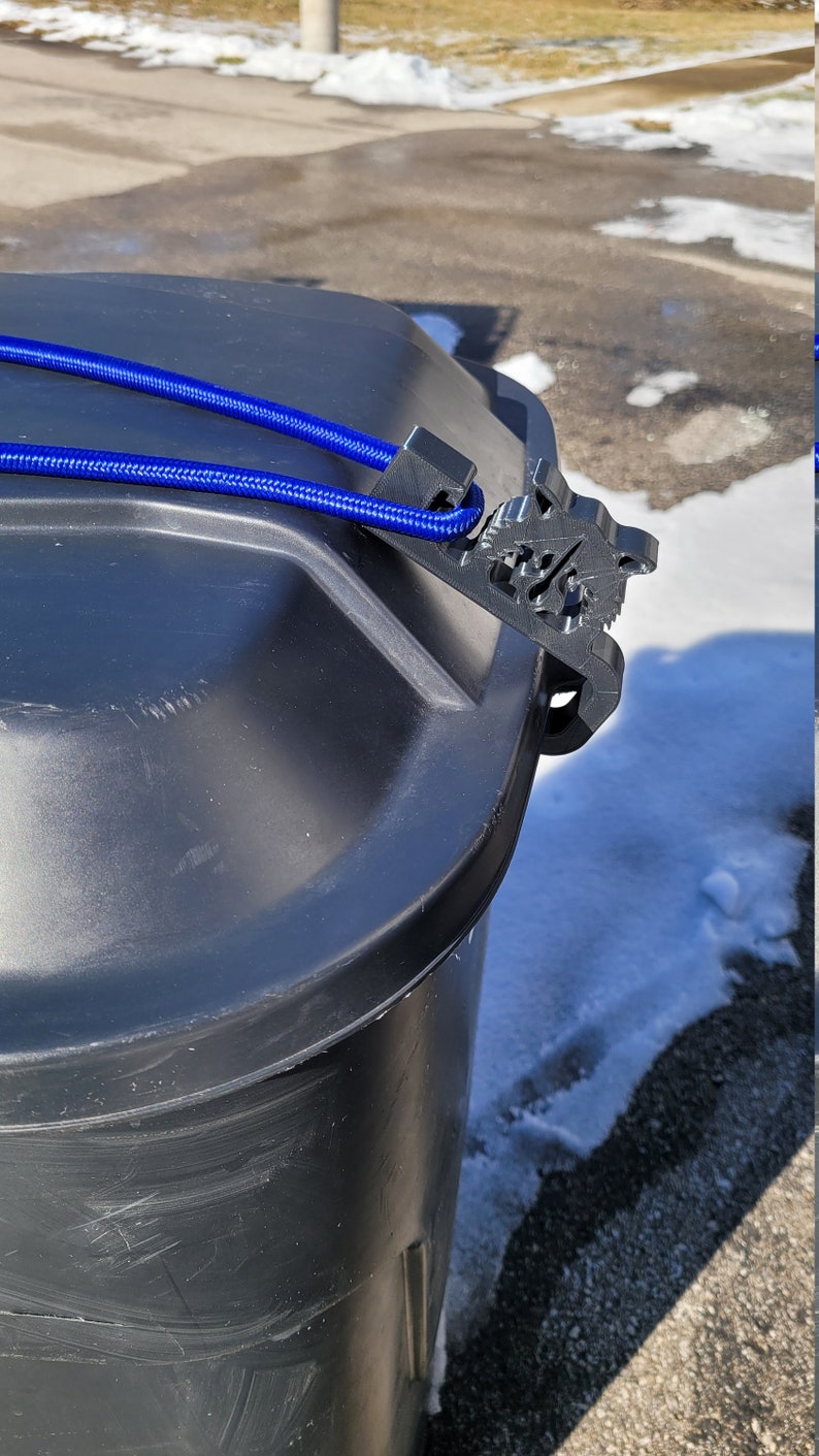 Puede incluir: Un cubo de basura de pl&aacute;stico negro con una cuerda azul atada alrededor de la tapa. La tapa tiene un cierre de pl&aacute;stico negro.