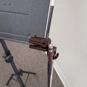May include: A brown music stand with a dark gray surface and a brown clip holding a pencil. The stand has a tripod base and a height-adjustable pole. The pencil has the text "0.7 mm" on it.