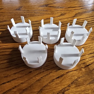 May include: Five white, circular, 3D-printed objects with a series of vertical supports around the perimeter. The objects are arranged on a wooden surface, with the lighting creating shadows and highlighting the texture of the wood.