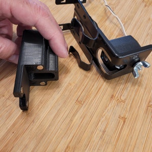 May include: Two black plastic camera mounts with metal parts. One mount has a small camera lens visible. The mounts are on a wooden surface.