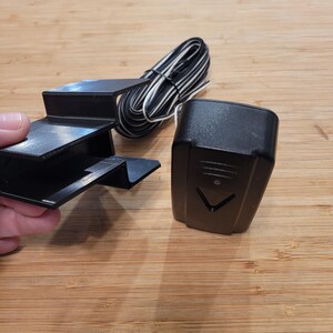 May include: A black wireless doorbell system with a small black receiver and a black mounting bracket. The system includes a white wire.