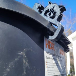 Puede incluir: Un elevador de tapa de contenedor de basura de pl&aacute;stico gris con el texto "HDX Rollout Trash Container Basurero con tapa basculante" en el lateral. El texto incluye caracter&iacute;sticas como "Ruedas de servicio pesado para una f&aacute;cil maniobrabilidad", "Bisagras duraderas que resisten los elementos", "Resistente al &oacute;xido y al polvo", "Dise&ntilde;o compacto y que ahorra espacio", "Las puntas estabilizan el contenedor durante la recolecci&oacute;n", "Resistente a las astillas y los ara&ntilde;azos", "21,2"An x 25,5"Al x 25,5"Pr".