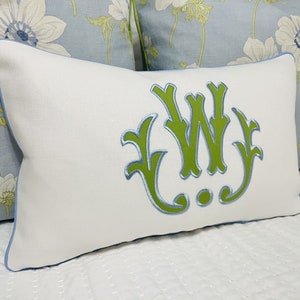 Op de afbeelding: Wit kussen met een lichtblauwe rand en een groen geborduurd monogram van de letters "W J".