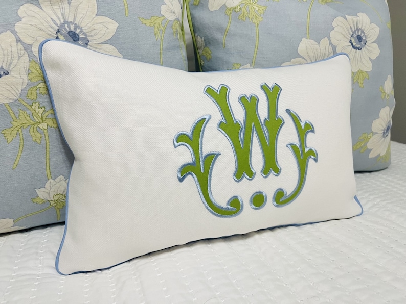 Op de afbeelding: Wit kussen met een lichtblauwe rand en een groen geborduurd monogram van de letters "W J".