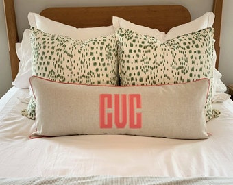 May include: A white bed with a white and green patterned pillow and a long, light-colored pillow with the initials "CVC" in pink.