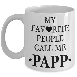 May include: White ceramic mug with a curved handle. The mug features black text that reads "MY FAVORITE PEOPLE CALL ME PAPP" with a black heart symbol and stars.