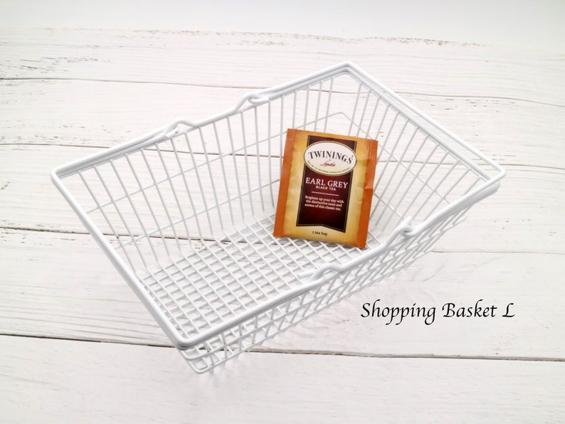 May include: White wire shopping basket with a single tea bag inside. The tea bag is labeled "Twinings Earl Grey Black Tea". The text "Shopping Basket L" is visible below the basket.