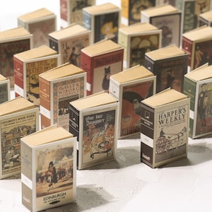 May include: A collection of miniature book-shaped boxes featuring various vintage book covers. The boxes are made from cardboard and have a rustic, antique look. The covers feature illustrations and text from classic books, such as "The True Mother Going", "The Avlt & Wiborg Company", "One Fair Daughter", and "Harper's Weekly".