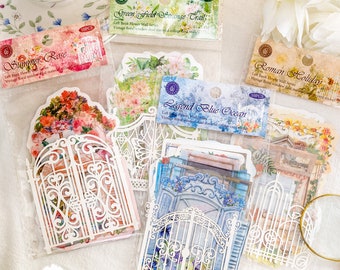 May include: A set of 10 decorative paper stickers featuring vintage floral designs and ornate gates. The stickers are packaged in clear plastic bags with labels that read "Summer Rose", "Green Field Strange Trail", "Legend Blue Ocean", and "Roman Holiday".