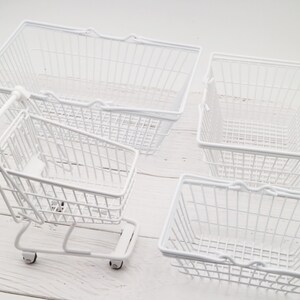 May include: Four white wire baskets, including a small shopping cart with wheels. The baskets are empty and have a white metal finish.