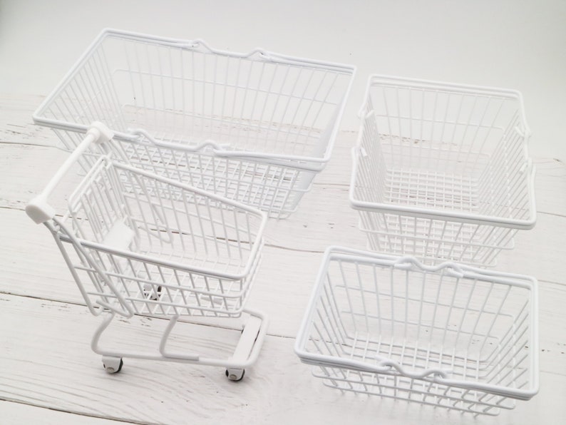 May include: Four white wire baskets, including a small shopping cart with wheels. The baskets are empty and have a white metal finish.