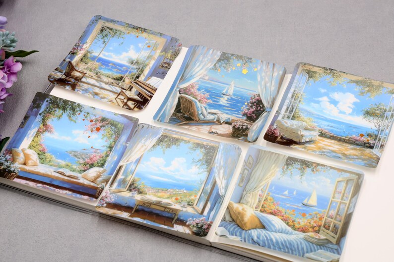 May include: A collection of six square art prints depicting serene coastal scenes viewed through open windows. Each print showcases a vibrant blue sky, ocean, and various outdoor settings with furniture and floral arrangements. The prints are arranged in an open book.