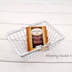 May include: White wire shopping basket with a single tea bag inside. The tea bag is labeled "Twinings of London Earl Grey Black Tea".