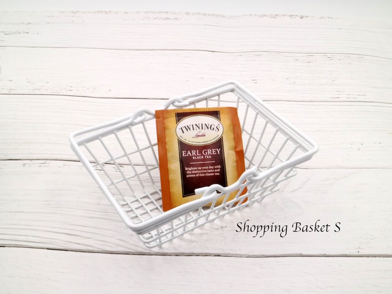 May include: White wire shopping basket with a single tea bag inside. The tea bag is labeled "Twinings of London Earl Grey Black Tea".