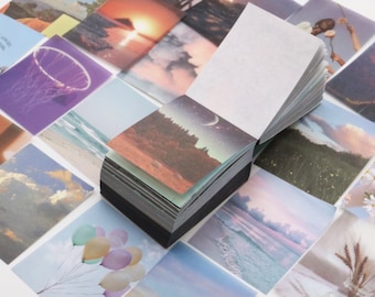 May include: A stack of colorful, square, paper note cards with various images, including a basketball hoop, a sunset, a beach, and a night sky. The cards are arranged in a grid pattern and are stacked on top of each other.