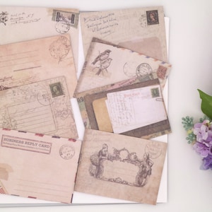 May include: A collection of vintage-style envelopes with various designs and stamps. The envelopes are in shades of brown, beige, and white, with some featuring floral patterns, birds, and other decorative elements. The envelopes are arranged on a white surface.