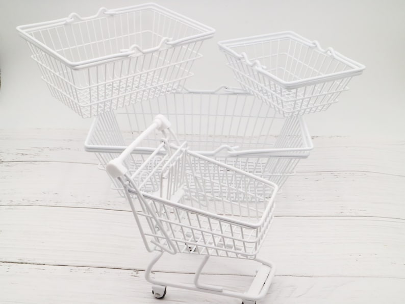 May include: Four white wire shopping baskets, one with wheels, stacked on a white wooden surface. The baskets are empty.