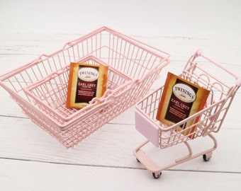 Puede incluir: Dos cestas de alambre rosa, una más grande que la otra, con un carrito de compras de alambre rosa más pequeño. La cesta más grande tiene dos bolsitas de té dentro, ambas etiquetadas como "Twinings Earl Grey Black Tea".