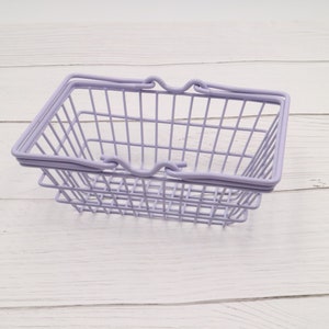 Puede incluir: Una cesta de la compra de alambre lavanda con un asa sobre una superficie de madera blanca.